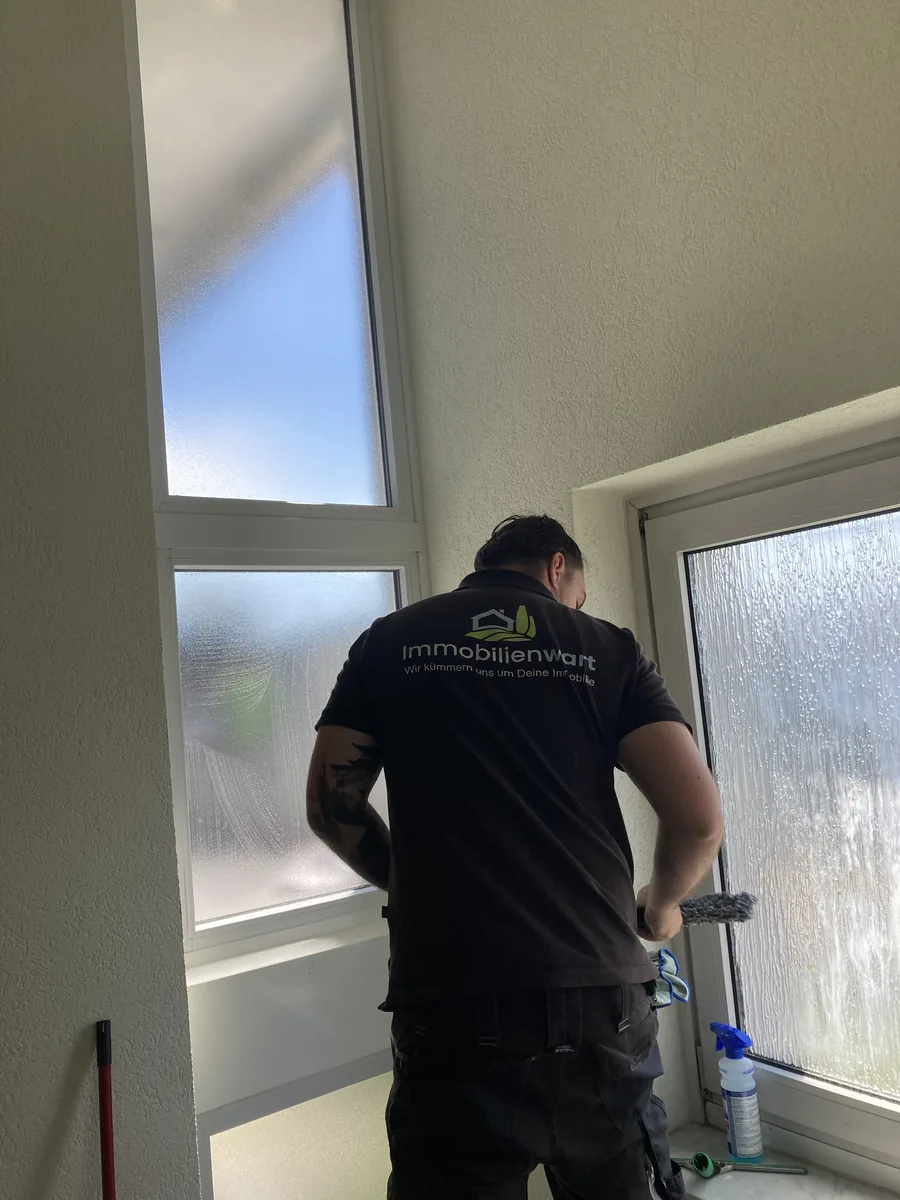 Mitarbeiter von Immobilienwart reinigt von hinten fotografiert ein Treppenhausfenster mit dem Abzieher