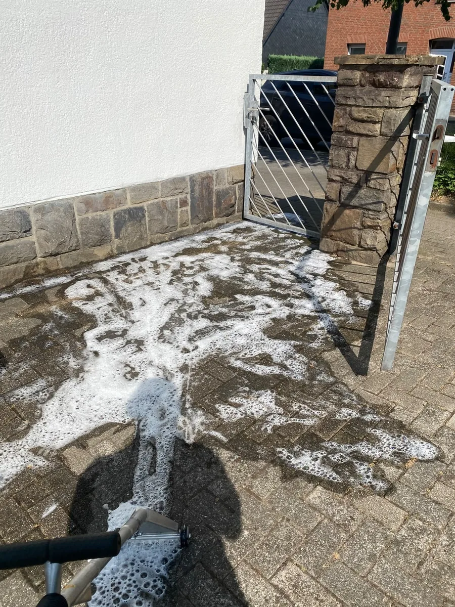 Gepflasterte Hofeinfahrt bei der Reinigung: Schaum auf dem Pflaster, Reinigungsgerät im Vordergrund