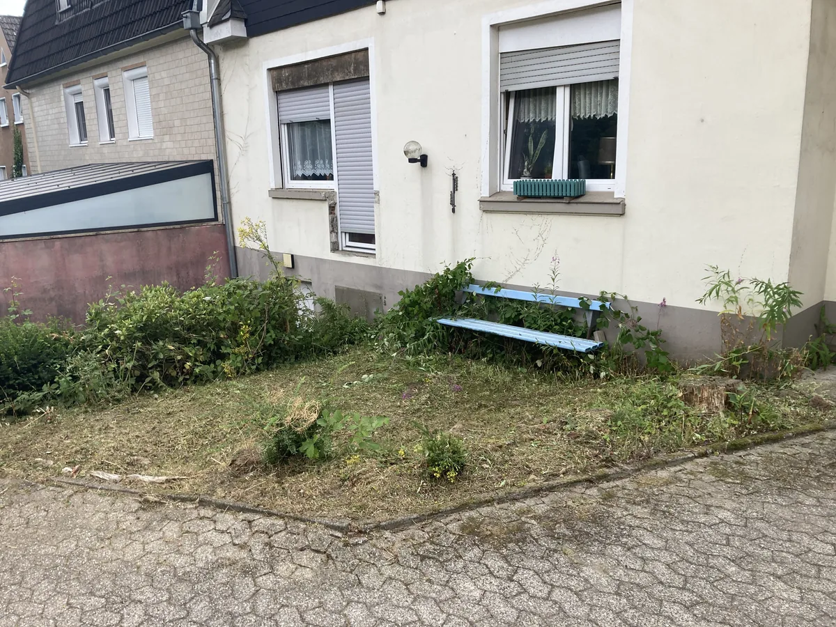 Derselbe Vorgarten nach der Pflege: Wildwuchs entfernt, Fläche abgeräumt, Bank an der Hauswand frei